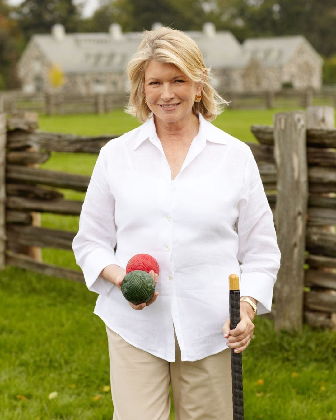 Martha Stewart v beli srajci pozira pred kamero z zelenjavo v rokah