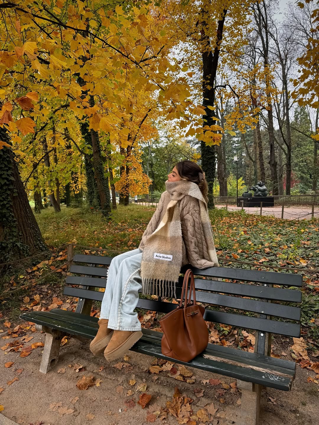 Ženska, ki sedi na klopci v Ugg škornjih sredi jesenskega parka