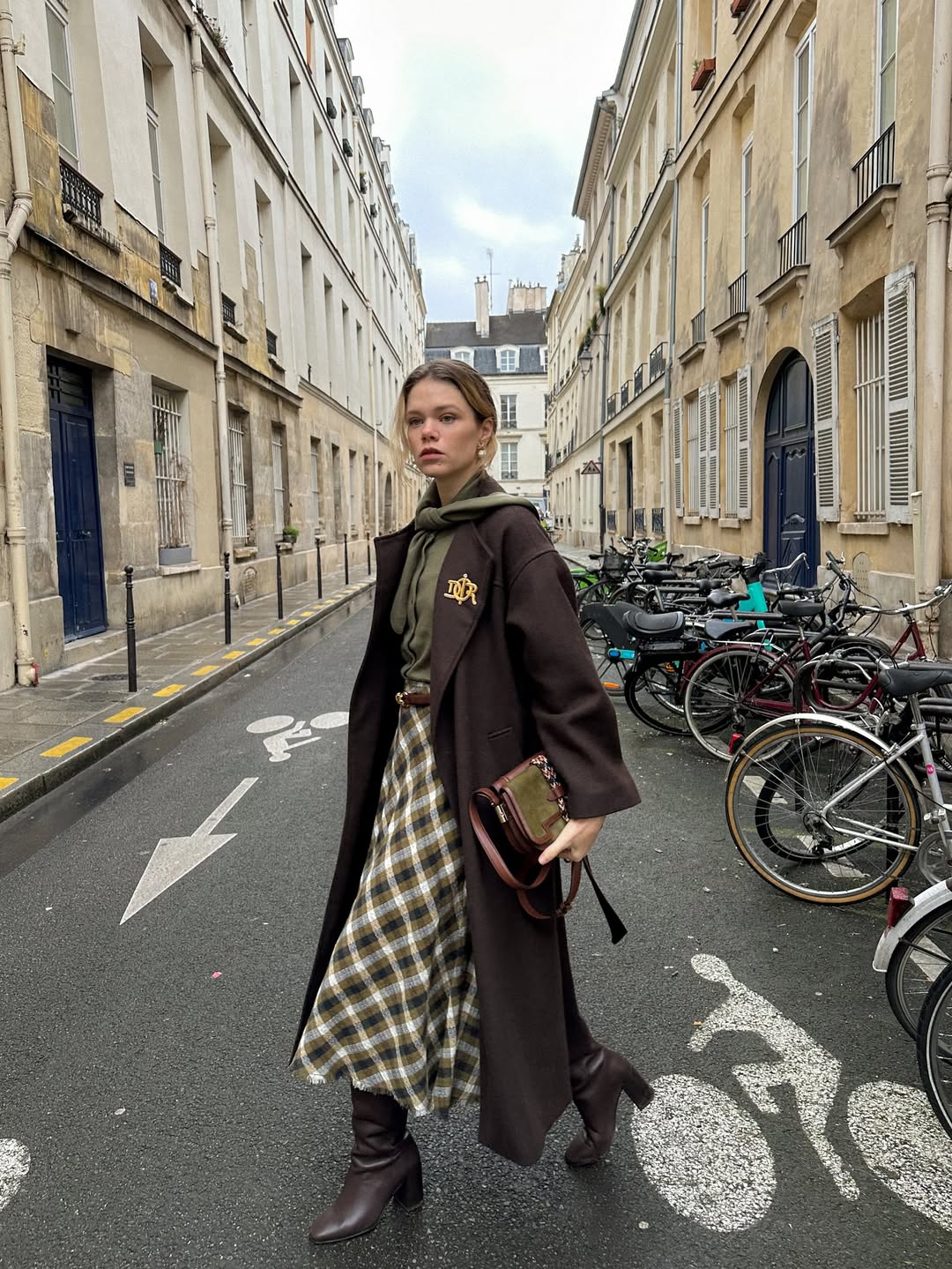 Ženska na ulici v daljšem plašču in karirastem krilu