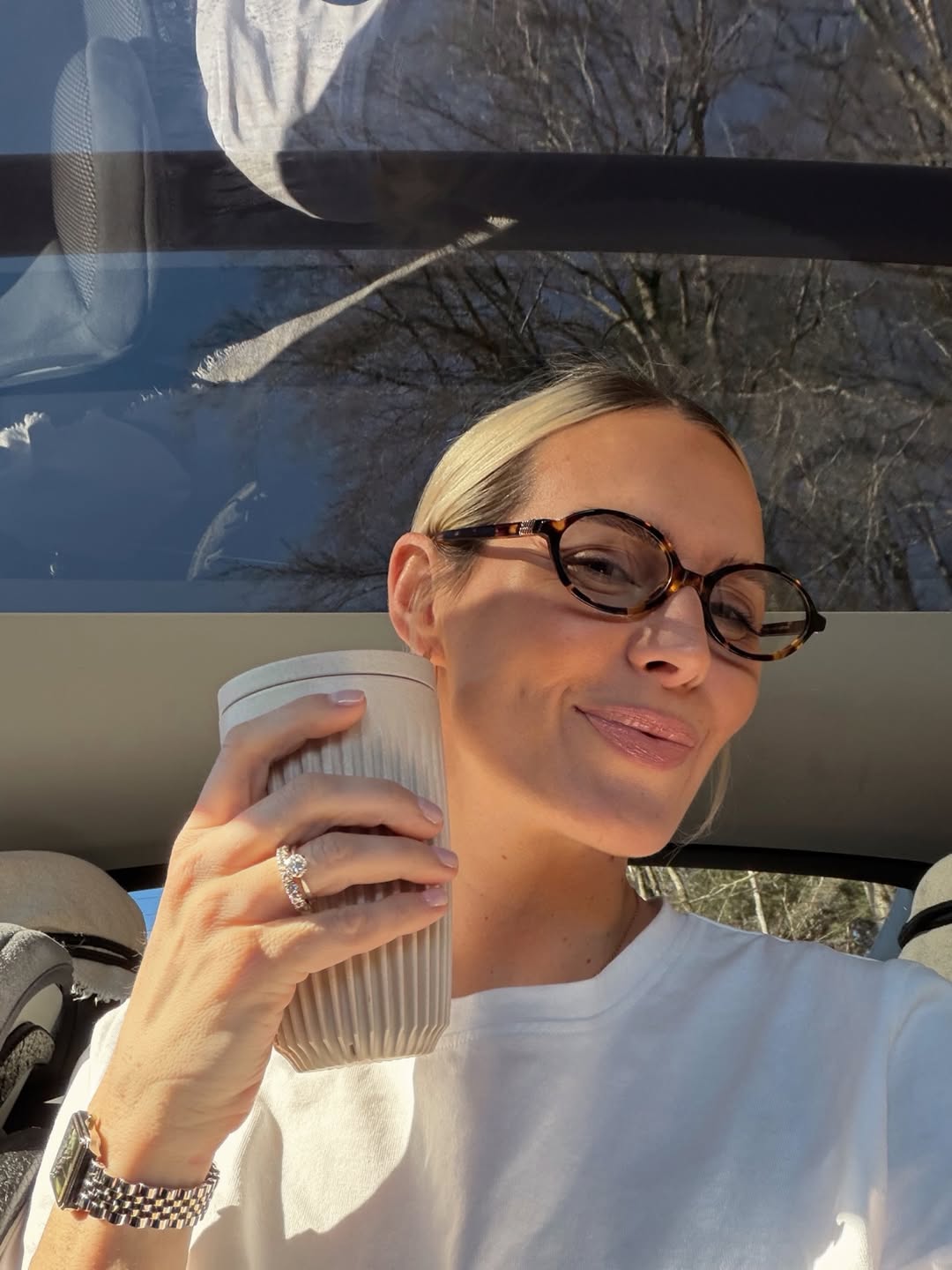 Ženska, ki se slika v avtu in v rokah drži kavo